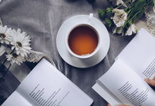 Overhead shot of tea in a white tea cup with two open books and white flowers around it.