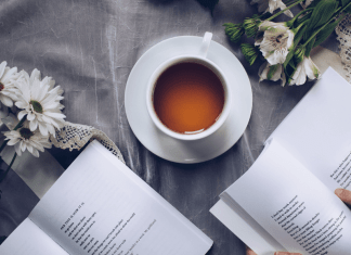 Overhead shot of tea in a white tea cup with two open books and white flowers around it.