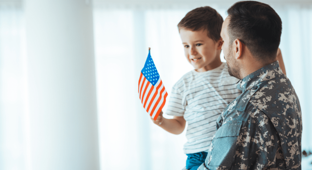 A veteran father carries his son who is holding an American flag.