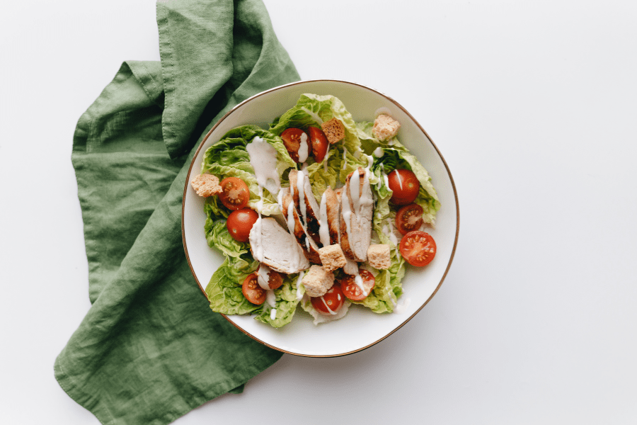 Bowl with salad and dressing sits on a green tea towel.