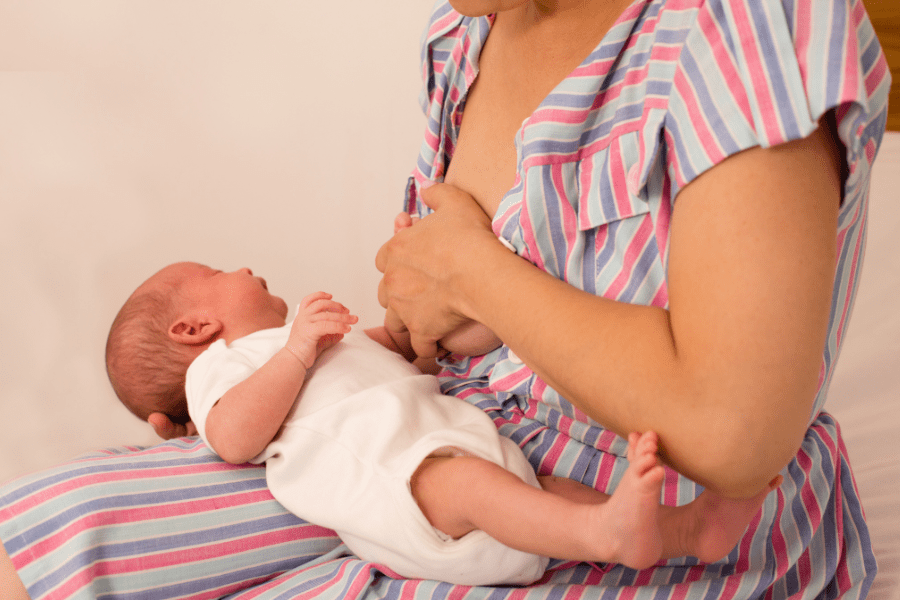 Mother holds breast while newborn cries. Both experience pain from thrush.