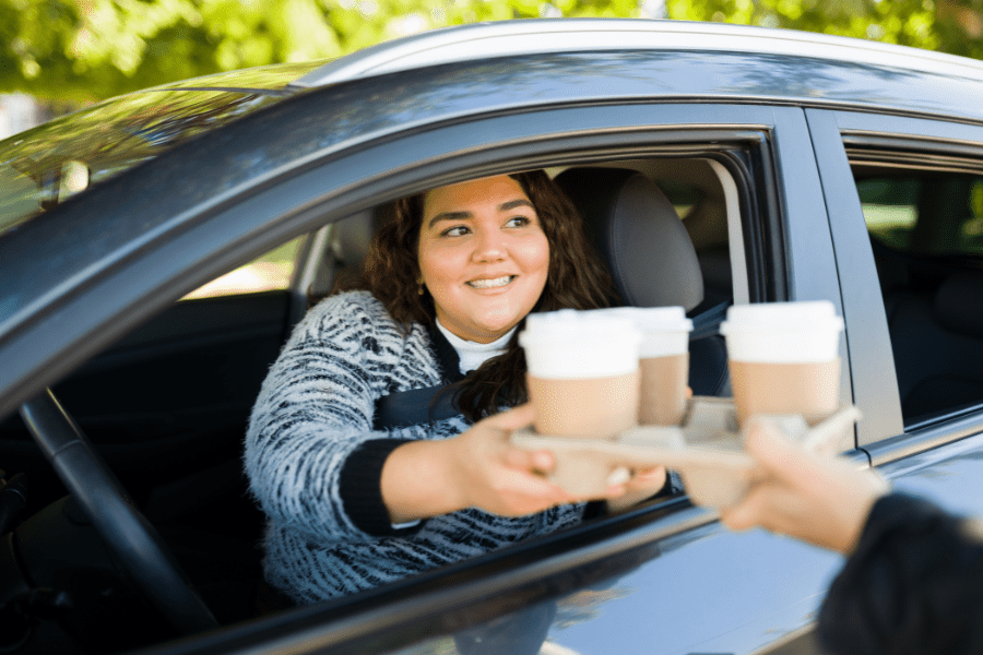 Woman receives tray of coffee drinks in her car at the drive-thru window.