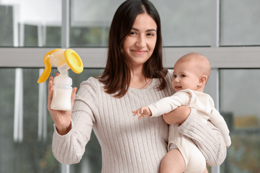 Mother holds baby in one arm and a breast pump bottle in her other hand.