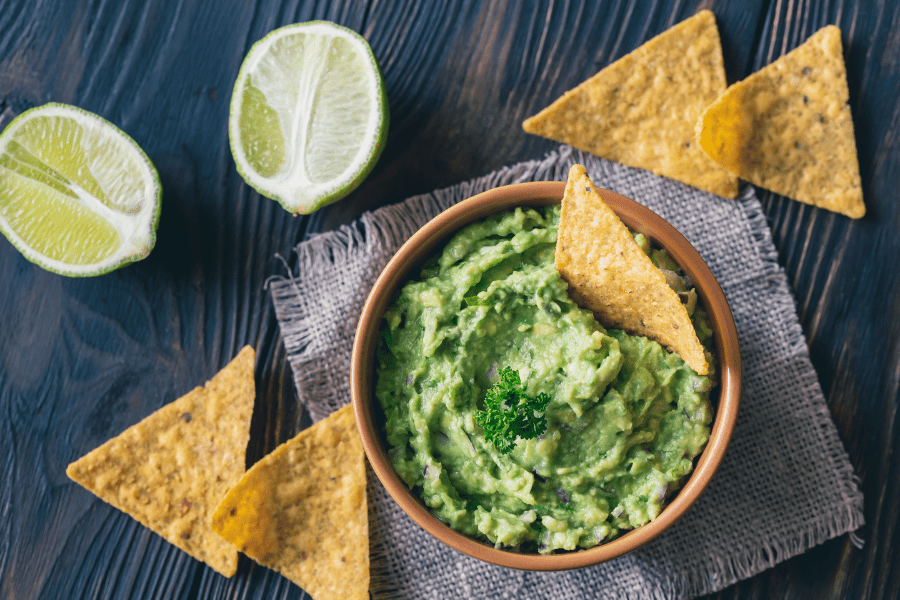 A side of chips and guacamole with lime wedges.