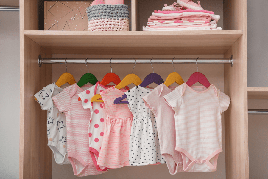 Cute baby dresses and bodysuits hanging up in a closet.