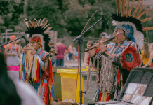 Native Americans play instruments in traditional attire.