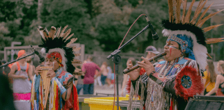 Native Americans play instruments in traditional attire.