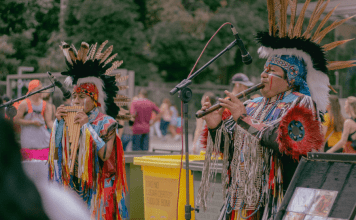 Native Americans play instruments in traditional attire.