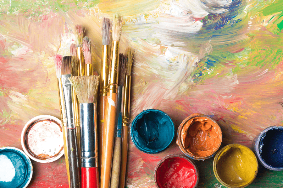 Paint brushes and pots of paint lay on an abstract painting.