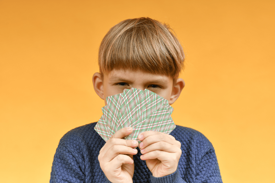 Little boy holds a hand of cards and squints skeptically at the camera