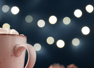 Mug of hot chocolate topped with marshmallows under some twinkle lights.