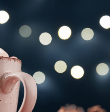 Mug of hot chocolate topped with marshmallows under some twinkle lights.