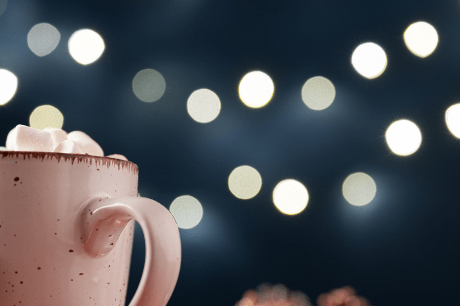 Mug of hot chocolate topped with marshmallows under some twinkle lights.